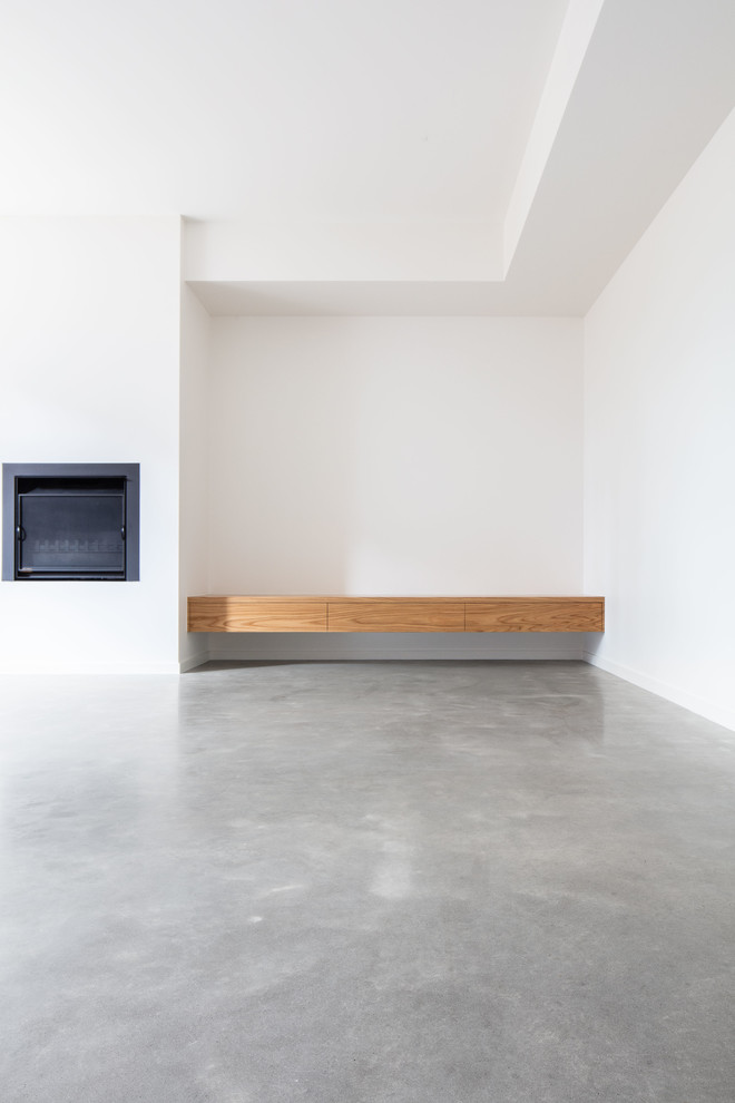 Imagen de sala de estar abierta contemporánea grande con paredes blancas, suelo de cemento, estufa de leña, marco de chimenea de metal y suelo gris