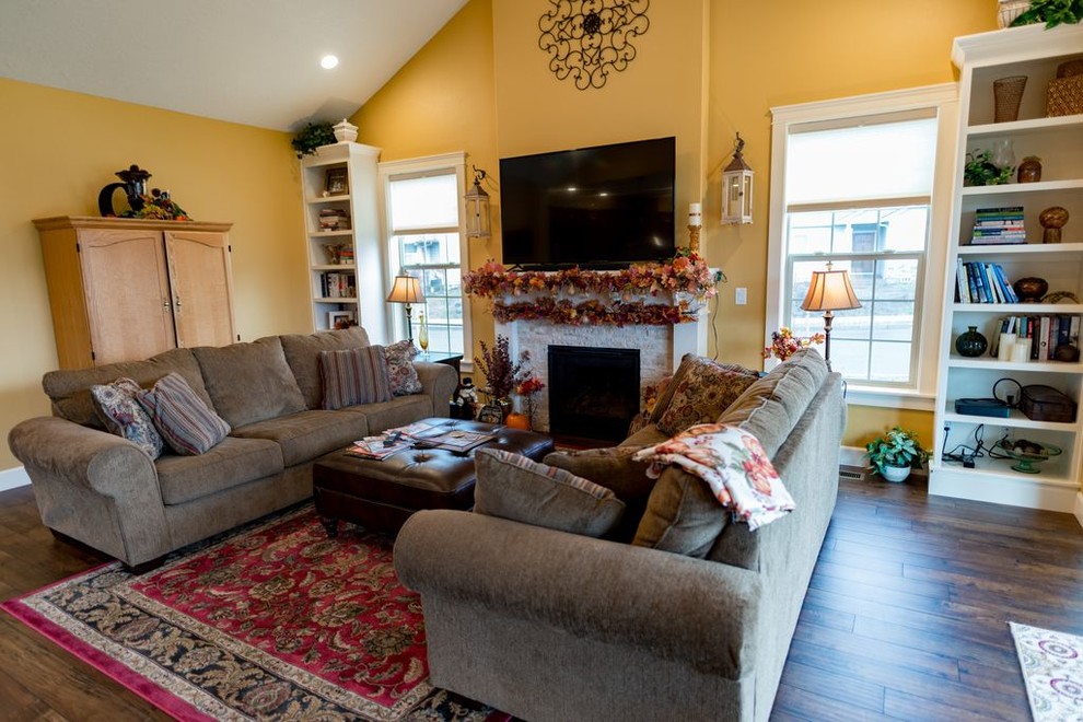 Foto de sala de estar abierta tradicional con paredes amarillas, todas las chimeneas, marco de chimenea de piedra, suelo marrón y televisor independiente