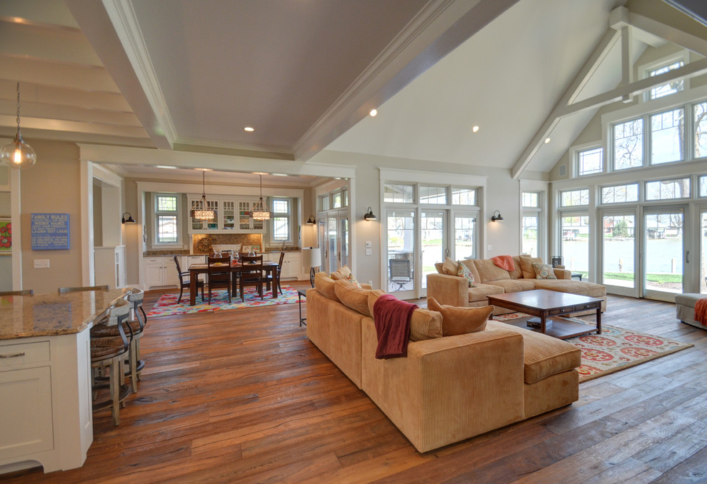 Imagen de sala de estar abierta de estilo americano grande con paredes beige, suelo de madera en tonos medios, todas las chimeneas y marco de chimenea de piedra