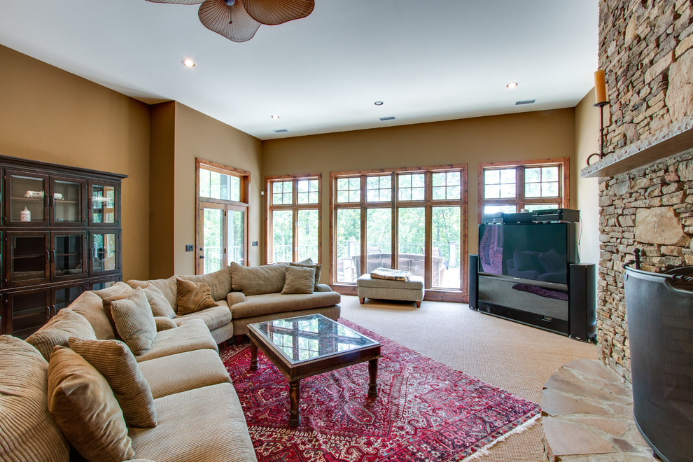 This is an example of a large rustic open plan games room in Nashville with a home bar, beige walls, carpet, a standard fireplace, a stone fireplace surround, a freestanding tv and beige floors.