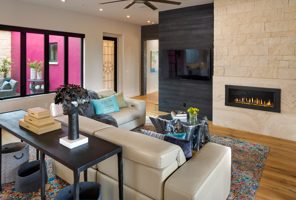 Cette image montre une salle de séjour sud-ouest américain avec un mur blanc, un sol en bois brun, une cheminée ribbon, un manteau de cheminée en pierre, un téléviseur fixé au mur et un sol marron.