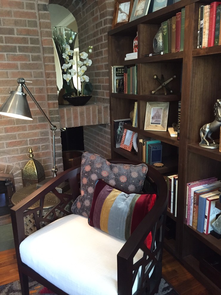 Cette image montre une petite salle de séjour vintage fermée avec une bibliothèque ou un coin lecture, un mur gris, un sol en bois brun, une cheminée double-face, un manteau de cheminée en brique et aucun téléviseur.