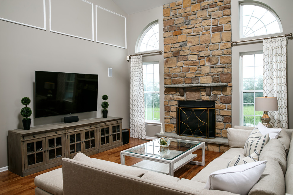 Cette image montre une salle de séjour minimaliste de taille moyenne et ouverte avec un mur gris, un sol en bois brun, une cheminée standard, un manteau de cheminée en pierre, un téléviseur fixé au mur et un sol marron.