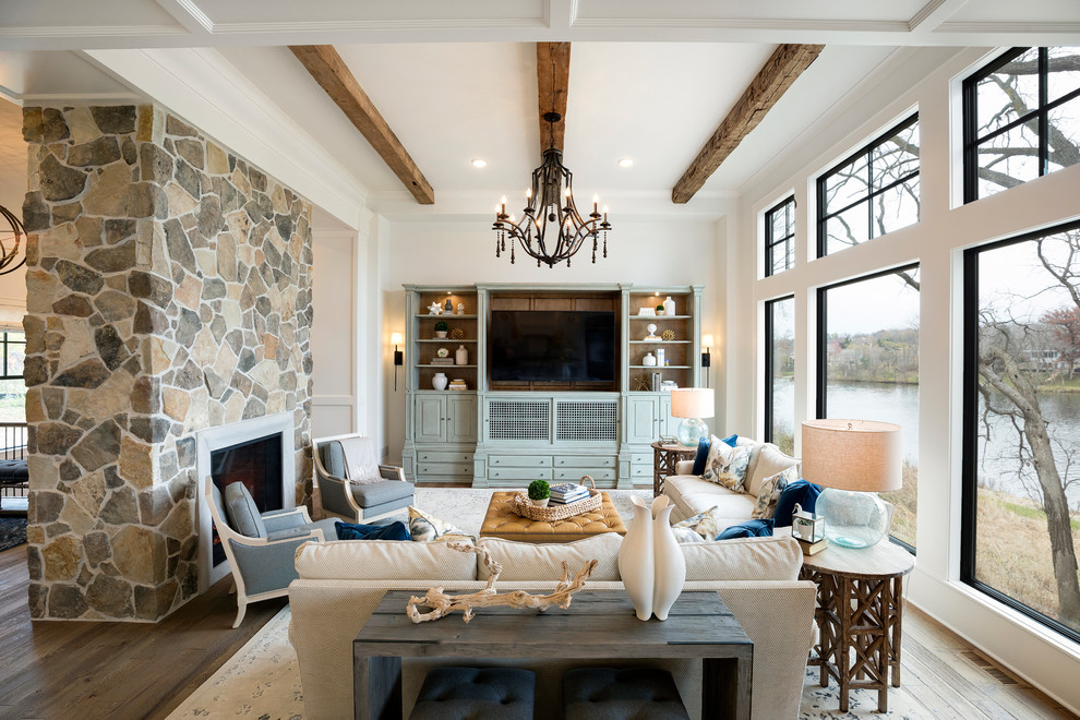Diseño de sala de estar abierta con paredes blancas, suelo de madera en tonos medios, chimenea de doble cara, marco de chimenea de piedra, pared multimedia y suelo marrón
