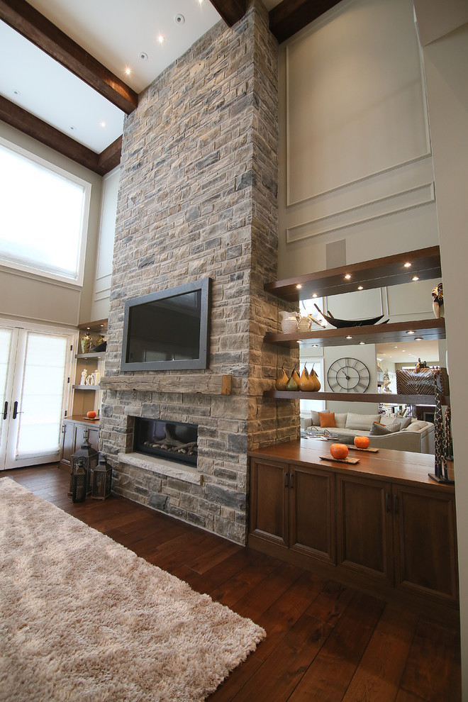 Foto de sala de estar abierta clásica renovada grande con paredes beige, suelo de madera en tonos medios, chimenea lineal, marco de chimenea de piedra y televisor colgado en la pared