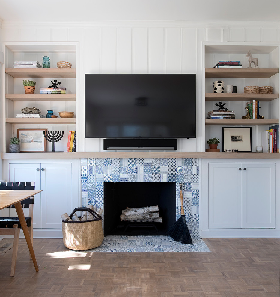 Imagen de sala de estar marinera con paredes blancas, suelo de madera en tonos medios, todas las chimeneas, marco de chimenea de baldosas y/o azulejos y televisor colgado en la pared