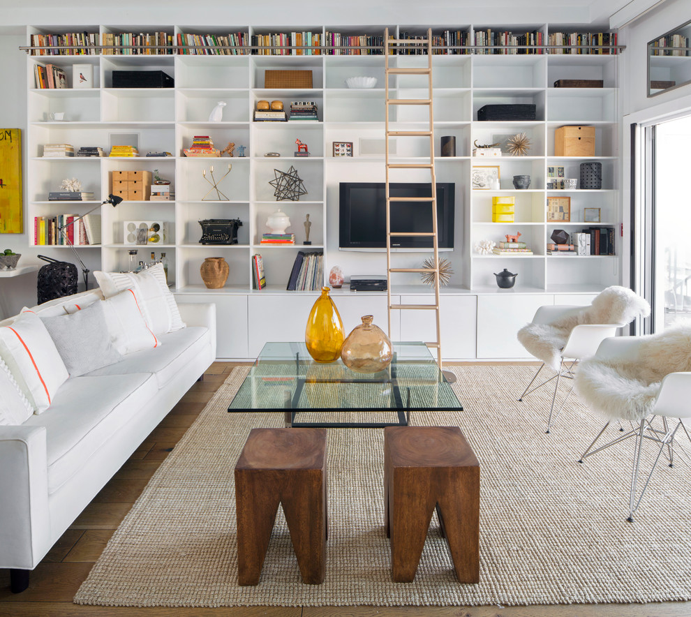 Imagen de sala de estar con biblioteca abierta actual grande sin chimenea con paredes blancas, suelo de madera clara, pared multimedia y alfombra
