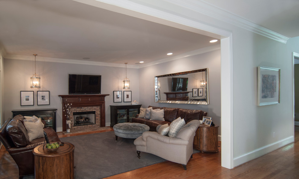 Imagen de sala de estar abierta clásica de tamaño medio con paredes grises, suelo de madera en tonos medios, todas las chimeneas, marco de chimenea de ladrillo y televisor colgado en la pared