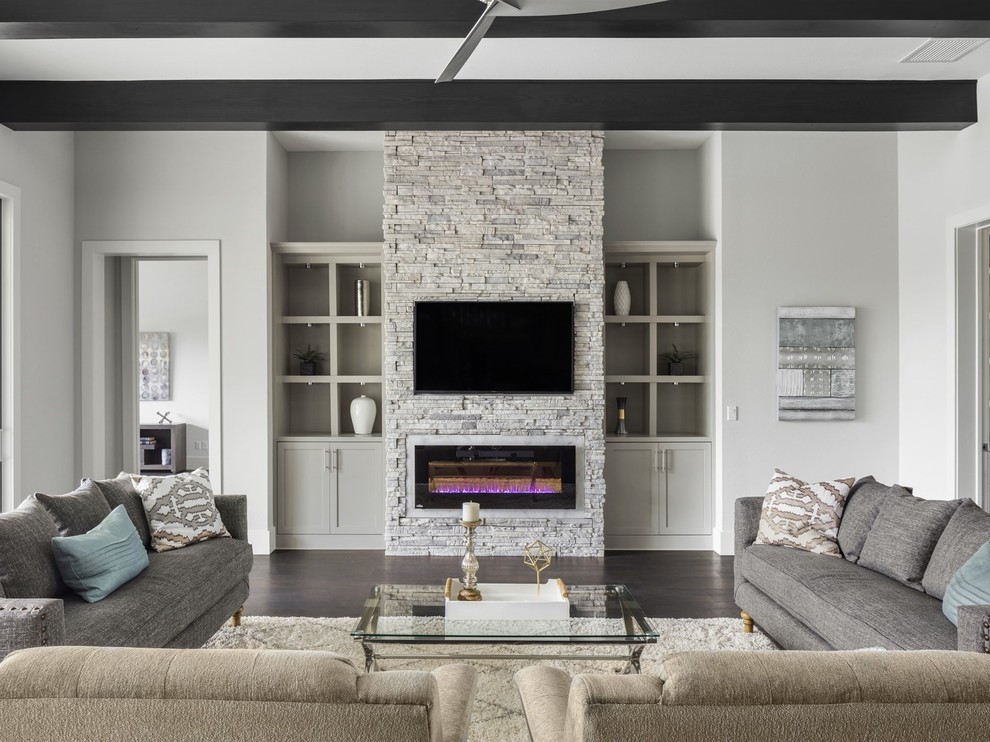 Diseño de sala de estar abierta clásica renovada grande con paredes grises, suelo de madera oscura, chimenea lineal, marco de chimenea de piedra, televisor colgado en la pared y suelo marrón