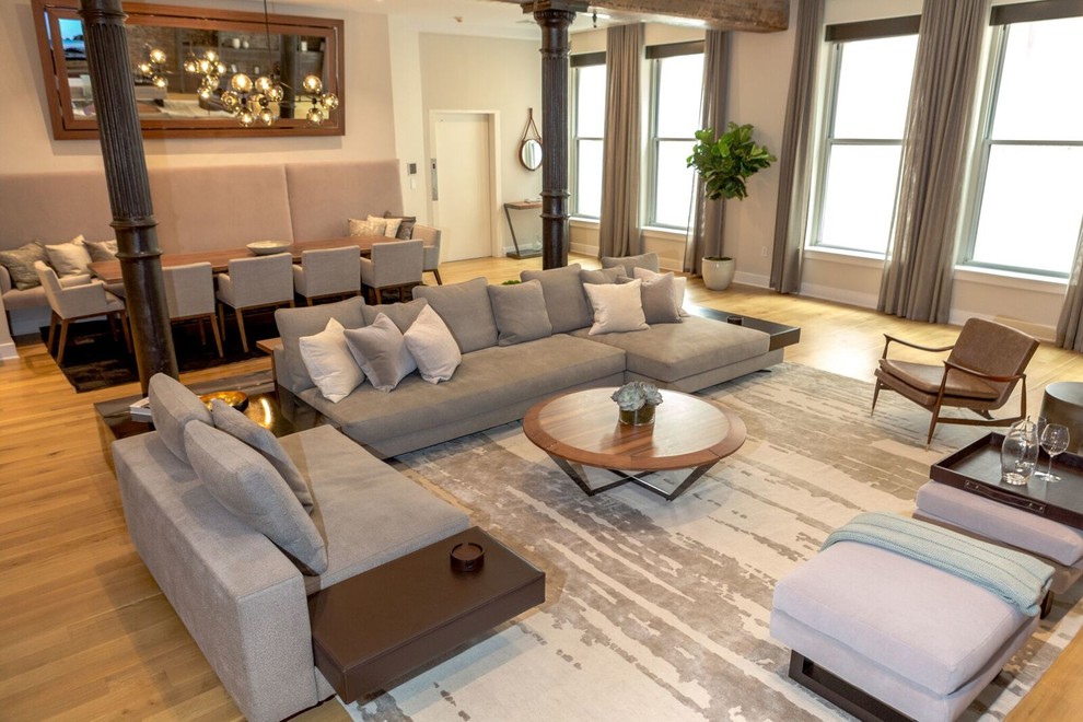 Modelo de sala de estar tipo loft contemporánea extra grande sin chimenea con suelo de madera clara, pared multimedia y paredes beige