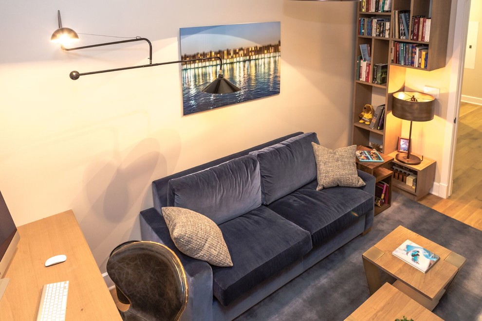 Modelo de sala de estar tipo loft actual grande sin chimenea con suelo de madera clara, pared multimedia y paredes beige