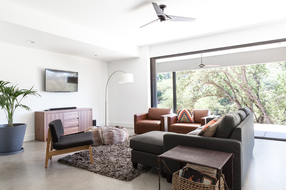 На фото: гостиная комната в современном стиле с белыми стенами, бетонным полом и телевизором на стене с