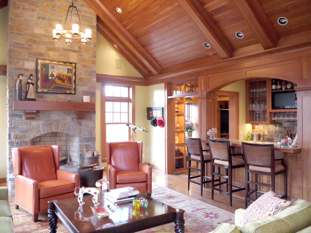 Modelo de sala de estar con barra de bar clásica con paredes beige, suelo de madera en tonos medios, todas las chimeneas, marco de chimenea de piedra y alfombra