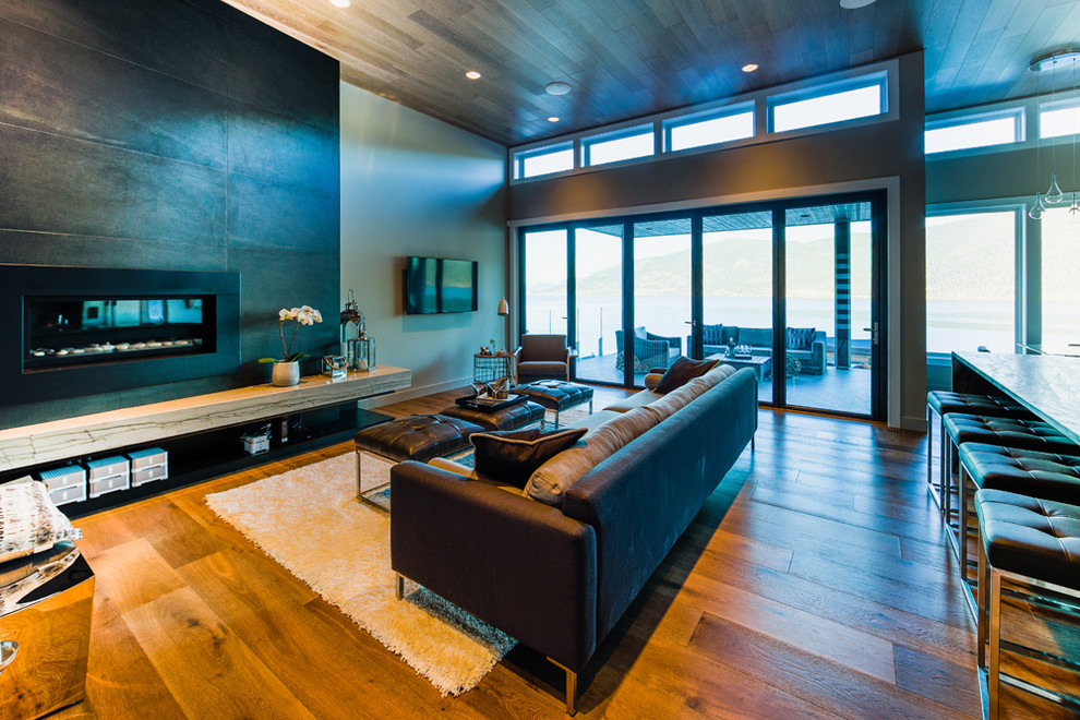 Imagen de sala de estar abierta contemporánea grande con paredes beige, suelo de madera clara, chimenea lineal, marco de chimenea de piedra y televisor colgado en la pared