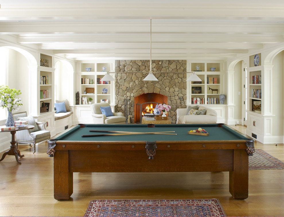 This is an example of a medium sized classic enclosed games room in Boston with a standard fireplace, a stone fireplace surround, light hardwood flooring, white walls, a concealed tv and brown floors.