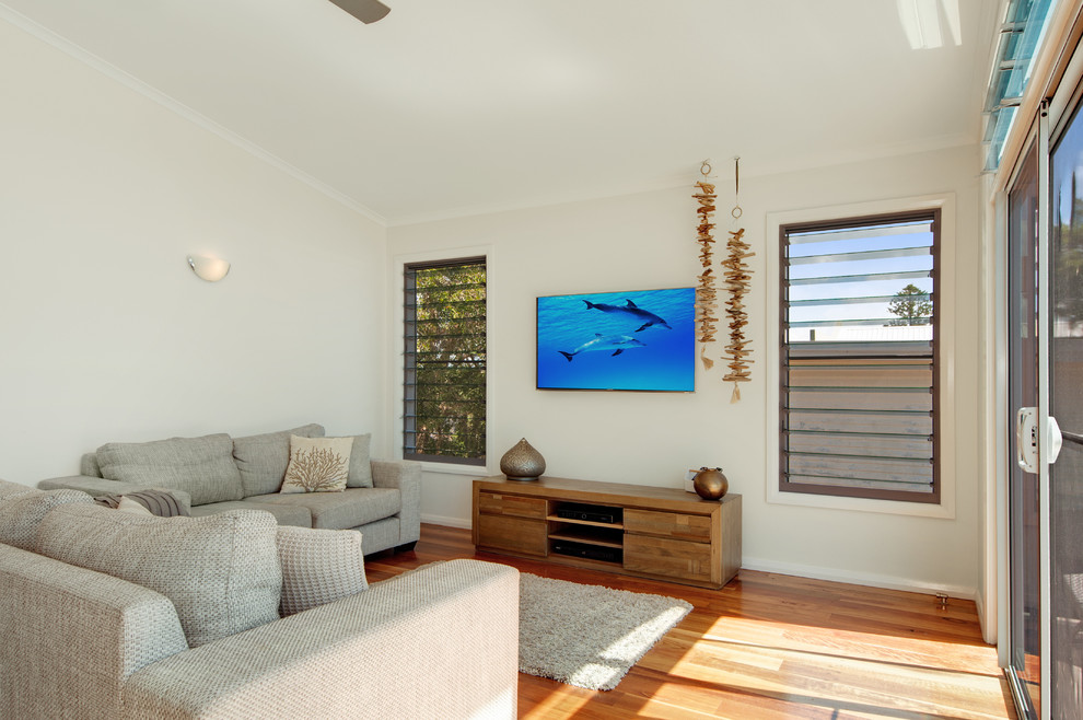 Imagen de sala de estar costera con paredes blancas, suelo de madera clara y televisor colgado en la pared