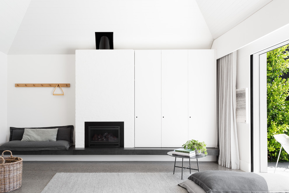 На фото: большая гостиная комната в стиле модернизм с белыми стенами, бетонным полом, стандартным камином, фасадом камина из кирпича и скрытым телевизором
