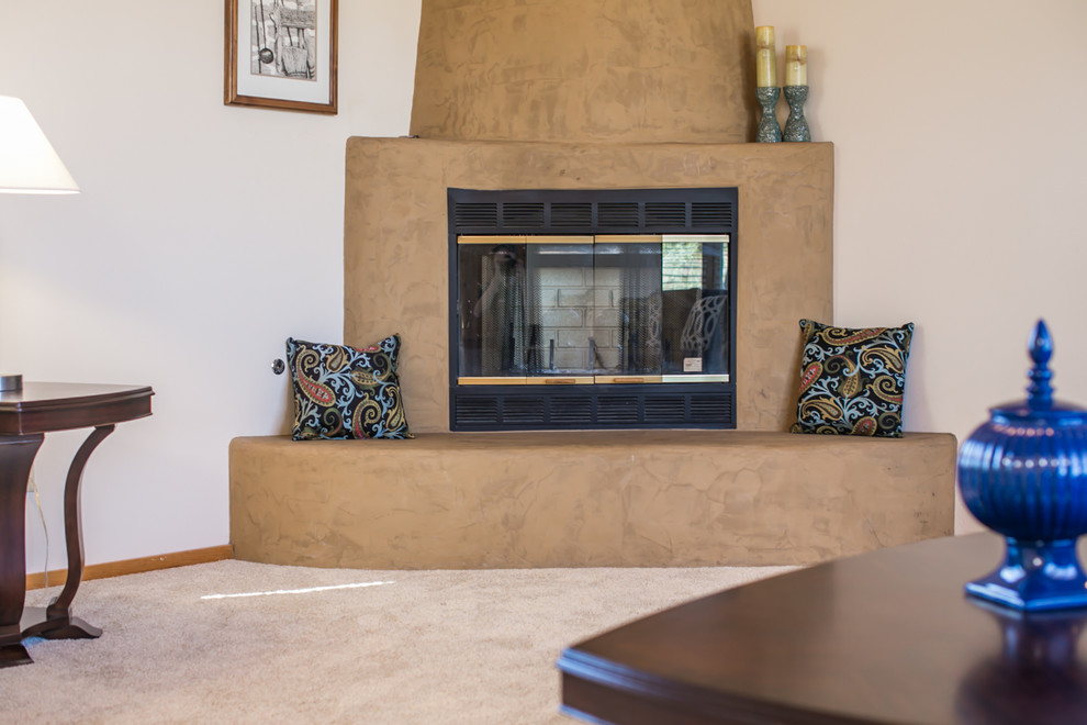 アルバカーキにあるラグジュアリーな広いサンタフェスタイルのおしゃれなオープンリビング (白い壁、カーペット敷き、コーナー設置型暖炉、漆喰の暖炉まわり、据え置き型テレビ) の写真