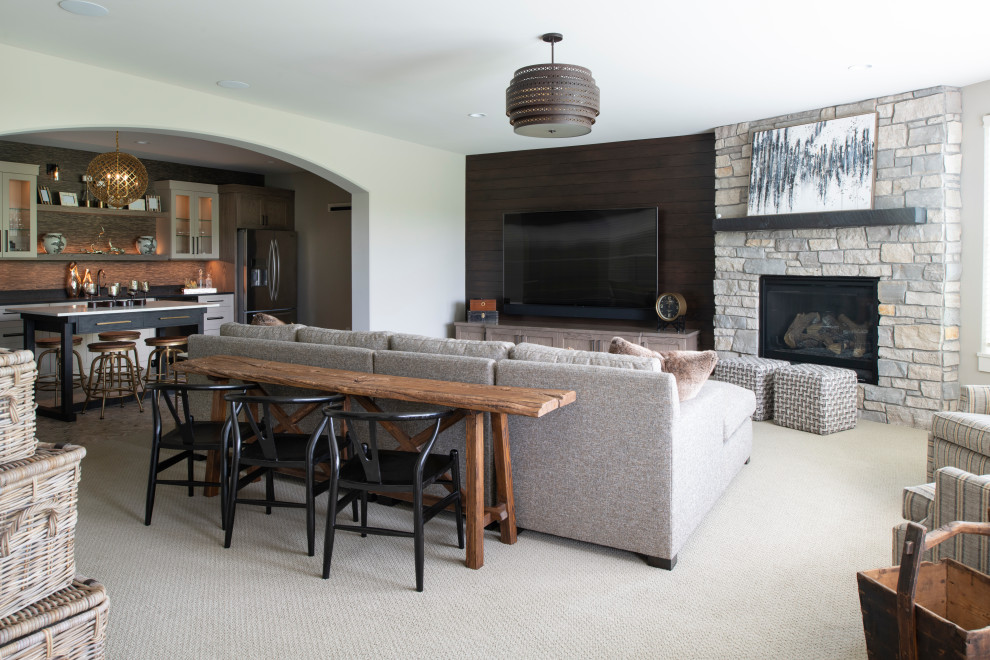 This is an example of a large open plan games room in Minneapolis with a home bar, grey walls, carpet, a standard fireplace, a stone fireplace surround, a wall mounted tv and grey floors.