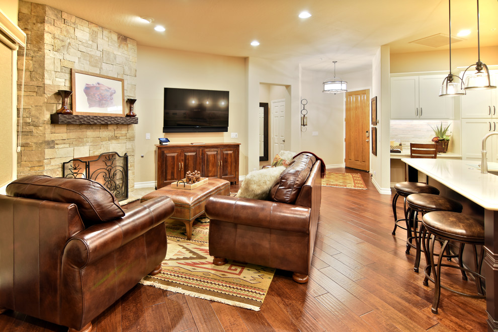 Foto de sala de estar abierta de estilo americano pequeña con paredes beige, suelo de madera oscura, chimenea de esquina, marco de chimenea de piedra y televisor colgado en la pared