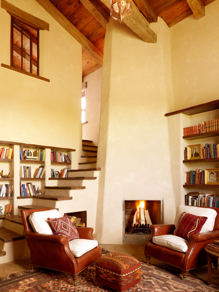 На фото: гостиная комната в средиземноморском стиле с с книжными шкафами и полками, бежевыми стенами и угловым камином с