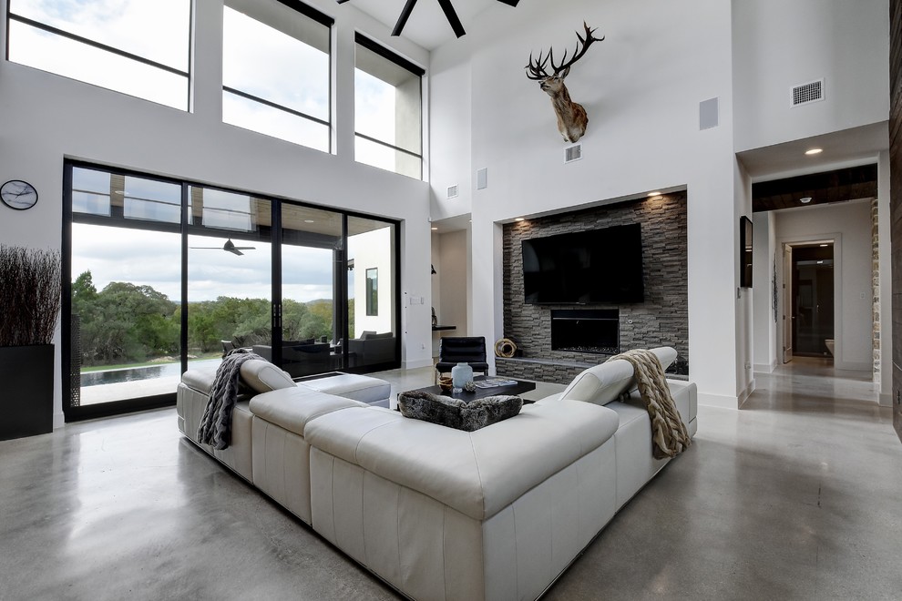 Diseño de sala de estar abierta contemporánea grande con paredes blancas, suelo de cemento, todas las chimeneas, marco de chimenea de baldosas y/o azulejos, televisor colgado en la pared y suelo gris