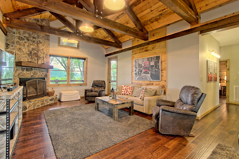 Medium sized rustic open plan games room in Other with grey walls, medium hardwood flooring, a corner fireplace, a stone fireplace surround, a freestanding tv and brown floors.