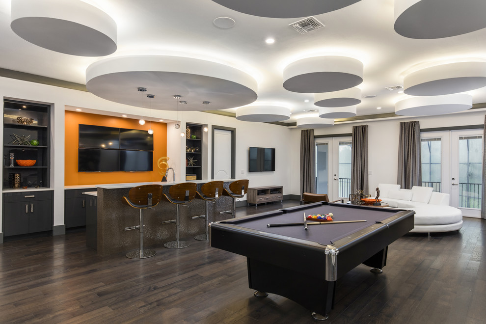 На фото: большая открытая гостиная комната в стиле модернизм с домашним баром, оранжевыми стенами, паркетным полом среднего тона и телевизором на стене без камина