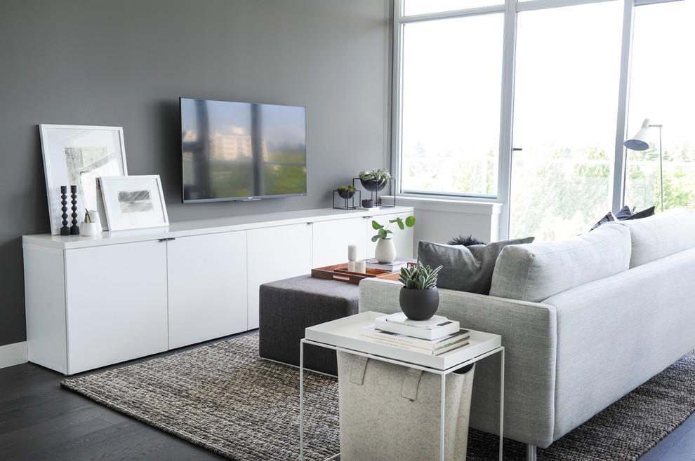 Imagen de sala de estar abierta actual pequeña sin chimenea con paredes grises, suelo de madera en tonos medios, televisor colgado en la pared y suelo gris