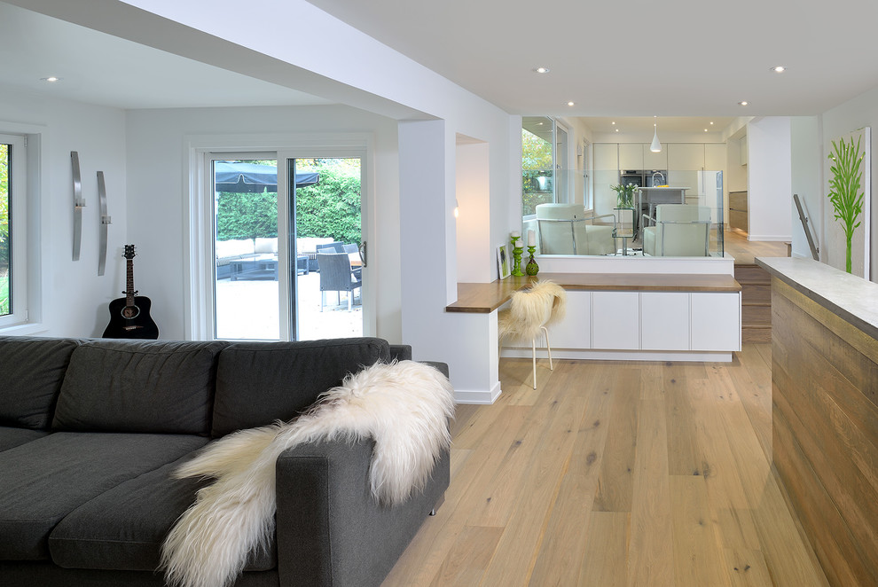 Imagen de sala de estar abierta contemporánea grande con paredes blancas, suelo de madera clara, marco de chimenea de ladrillo y pared multimedia