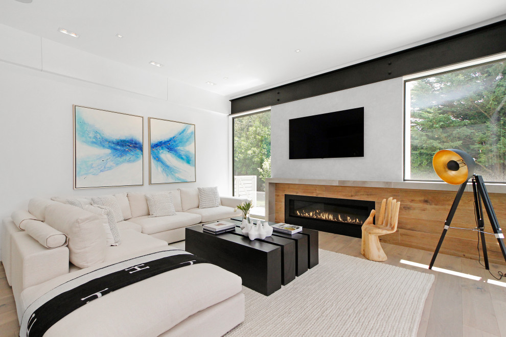 Imagen de sala de estar actual grande con paredes blancas, suelo de madera clara, chimeneas suspendidas, marco de chimenea de madera y suelo beige