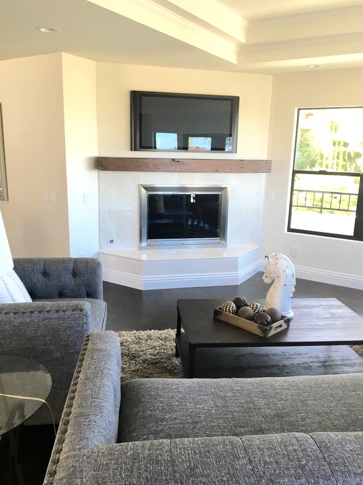サンディエゴにある高級な中くらいな地中海スタイルのおしゃれなオープンリビング (白い壁、濃色無垢フローリング、コーナー設置型暖炉、タイルの暖炉まわり、壁掛け型テレビ、茶色い床) の写真