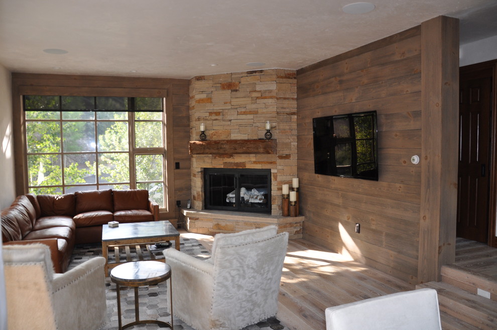Imagen de sala de estar abierta rústica grande con suelo de madera clara, todas las chimeneas, marco de chimenea de piedra y televisor colgado en la pared