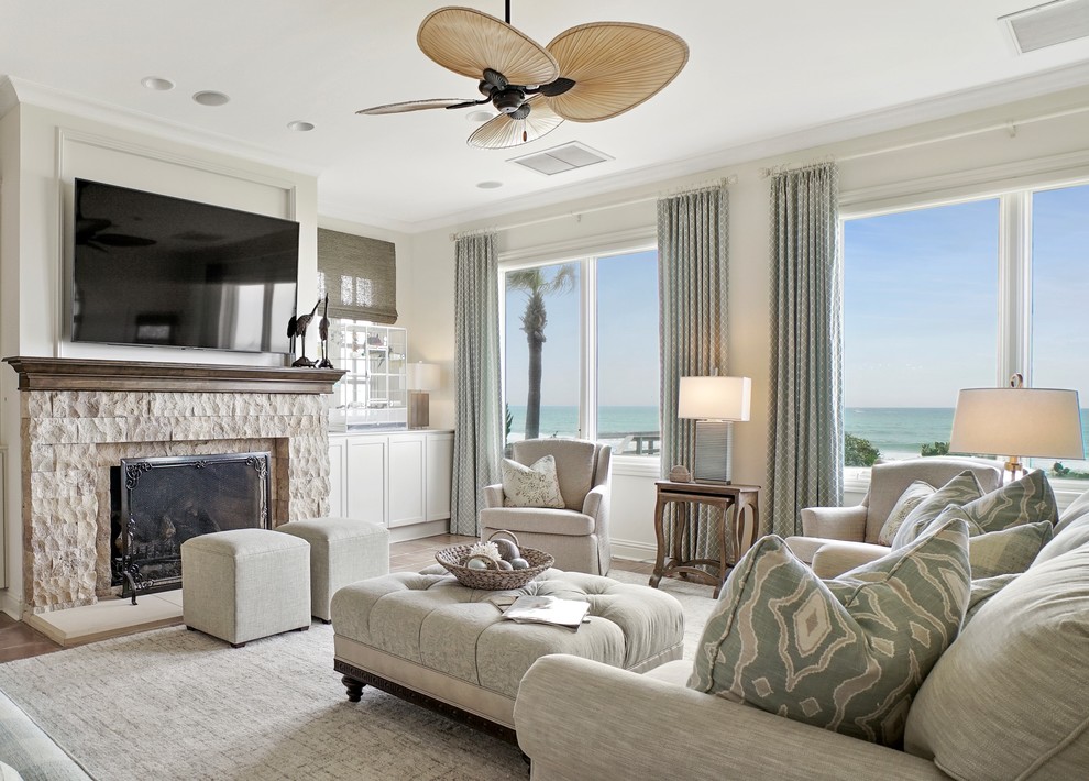 ジャクソンビルにある高級なビーチスタイルのおしゃれな独立型リビング (白い壁、標準型暖炉、石材の暖炉まわり、壁掛け型テレビ、グレーの床、セラミックタイルの床) の写真