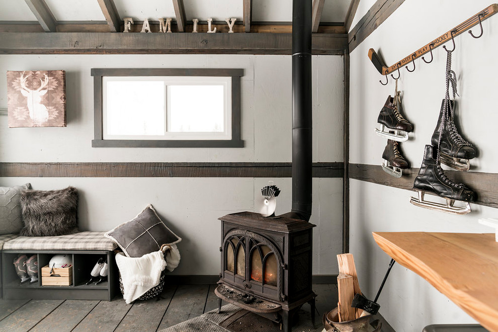 На фото: гостиная комната в стиле рустика с белыми стенами, деревянным полом, печью-буржуйкой и серым полом с