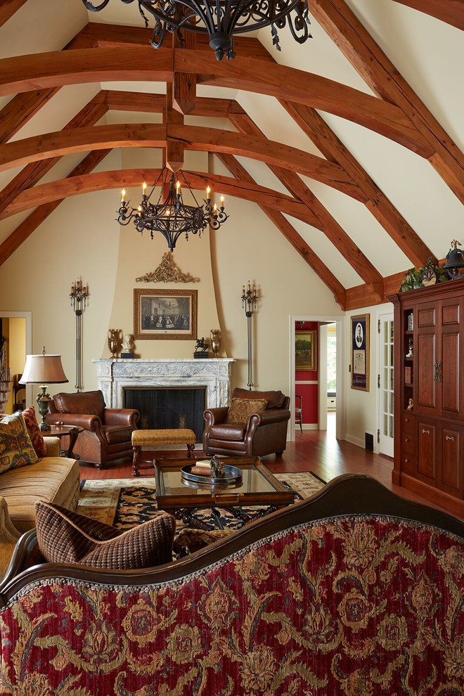 Cette photo montre une grande salle de séjour chic ouverte avec un mur beige, un sol en bois brun, une cheminée standard, un manteau de cheminée en pierre, aucun téléviseur et un sol marron.