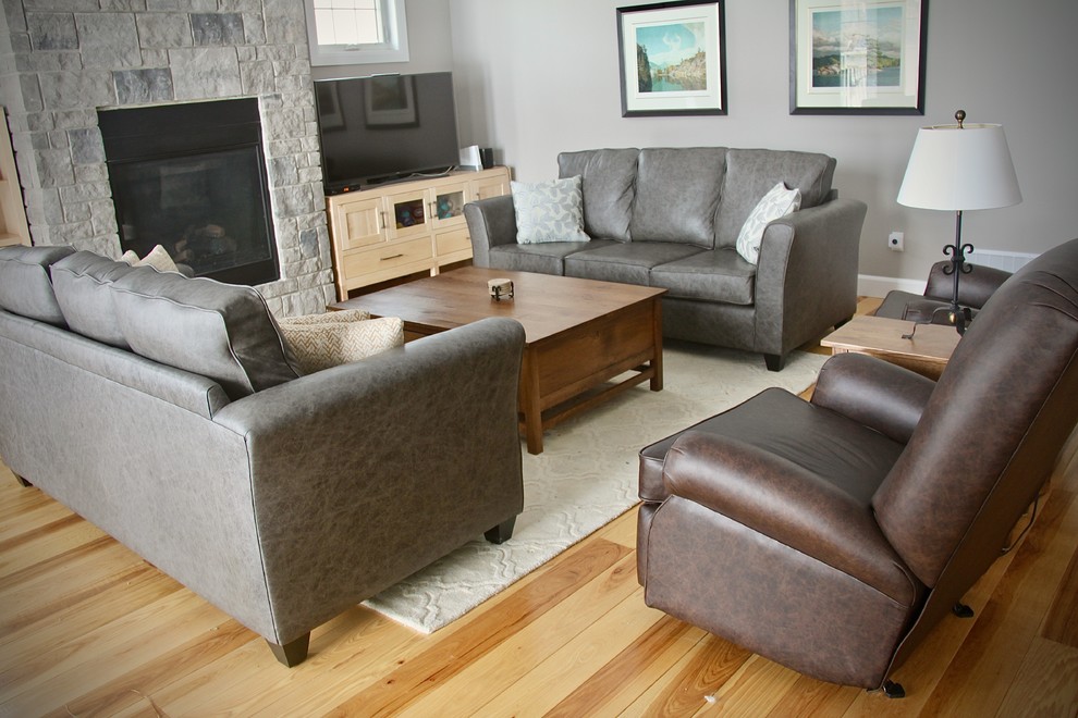 Offenes Wohnzimmer mit grauer Wandfarbe, hellem Holzboden, Kamin, Kaminumrandung aus Stein und Eck-TV in Toronto