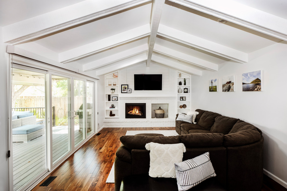 Design ideas for a contemporary games room in Denver with white walls, dark hardwood flooring, a standard fireplace, a brick fireplace surround, a wall mounted tv, brown floors and a vaulted ceiling.
