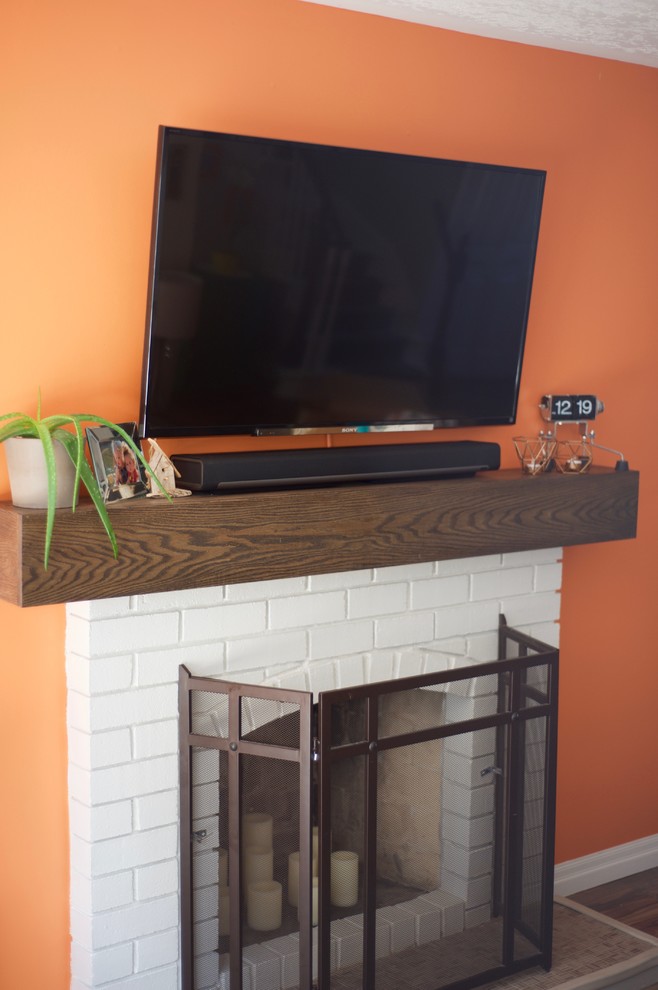 Modelo de sala de estar abierta retro pequeña con parades naranjas, todas las chimeneas, marco de chimenea de ladrillo y televisor colgado en la pared