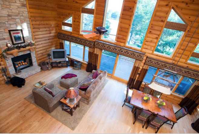 Modelo de sala de estar tipo loft rústica con paredes marrones, suelo de madera clara, todas las chimeneas y marco de chimenea de piedra