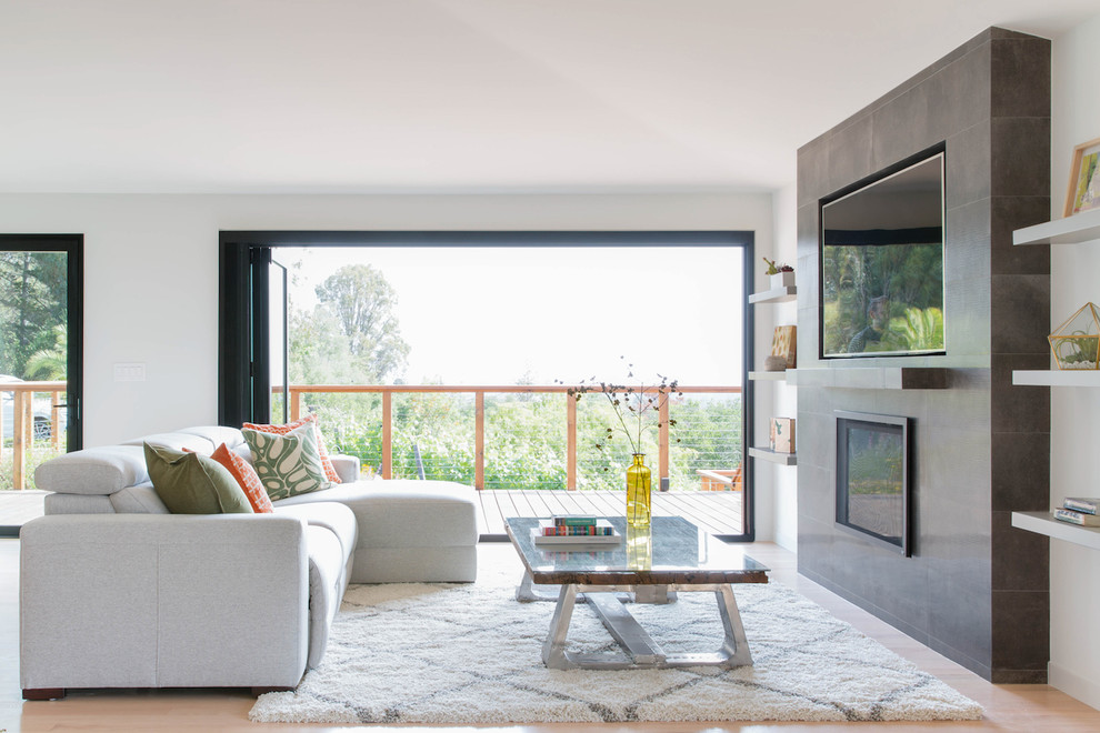 Cette image montre une salle de séjour design avec un mur blanc, parquet clair, une cheminée standard, un manteau de cheminée en carrelage, un téléviseur fixé au mur et un sol beige.