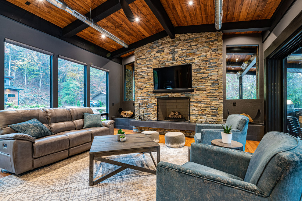 Large contemporary open plan games room in Raleigh with a stone fireplace surround, a wall mounted tv, grey walls, medium hardwood flooring, a standard fireplace and brown floors.