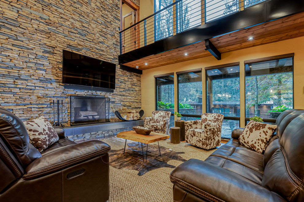 This is an example of a large rustic open plan games room in Raleigh with beige walls, medium hardwood flooring, a standard fireplace, a stone fireplace surround, a wall mounted tv and brown floors.