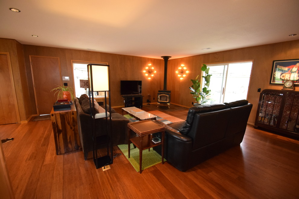 Пример оригинального дизайна: большая изолированная гостиная комната в стиле ретро с коричневыми стенами, полом из бамбука, печью-буржуйкой, фасадом камина из камня и коричневым полом