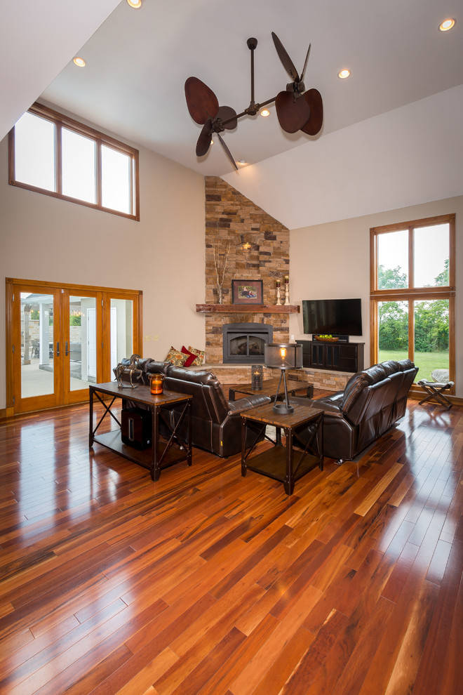 This is an example of a large rustic enclosed games room in Columbus with beige walls, medium hardwood flooring, a corner fireplace, a stone fireplace surround and a freestanding tv.