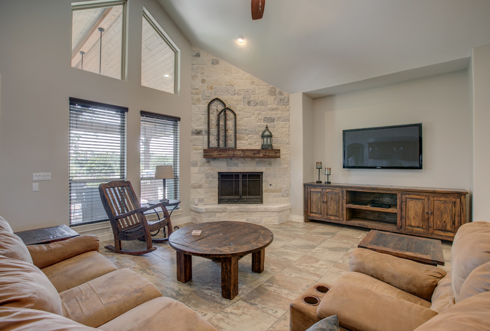 Inspiration for a large mediterranean enclosed games room in Austin with grey walls, porcelain flooring, a corner fireplace, a stone fireplace surround, a wall mounted tv and brown floors.