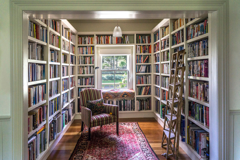 Réalisation d'une salle de séjour tradition avec une bibliothèque ou un coin lecture, un mur blanc, un sol en bois brun et un sol marron.