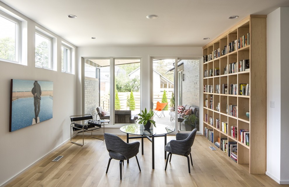 Ispirazione per un soggiorno design di medie dimensioni e aperto con libreria, pareti bianche e parquet chiaro