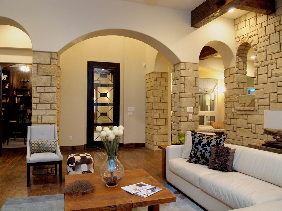 На фото: открытая гостиная комната среднего размера в средиземноморском стиле с телевизором на стене, белыми стенами, паркетным полом среднего тона, угловым камином и фасадом камина из камня