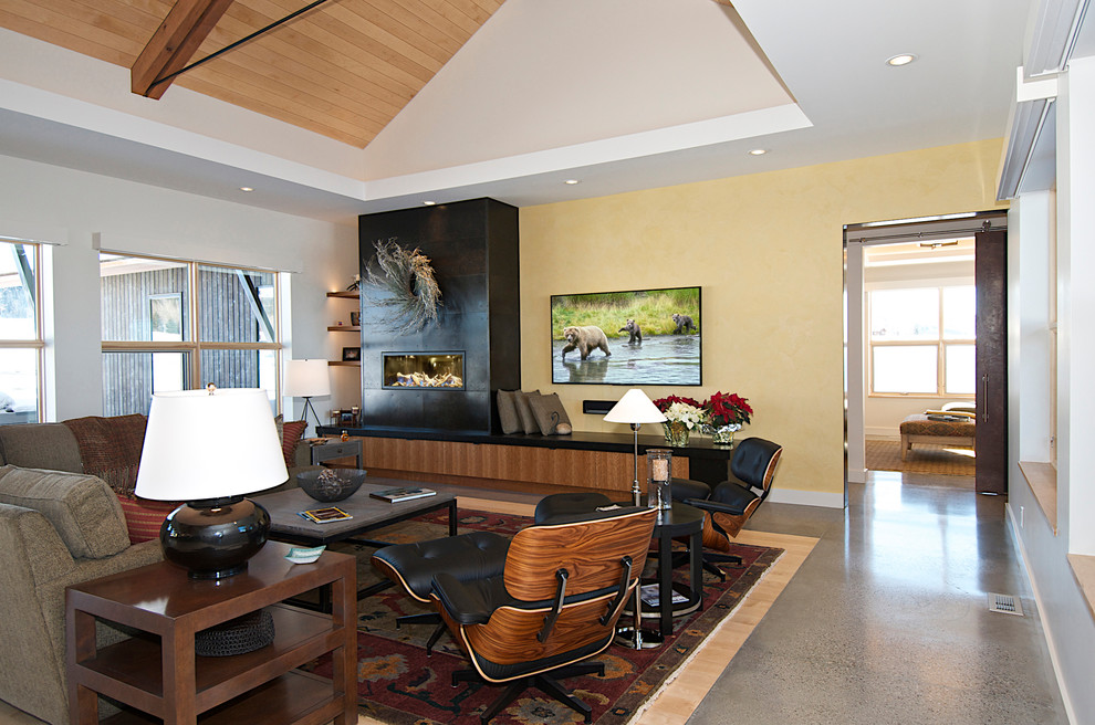 Mittelgroßes, Offenes Modernes Wohnzimmer mit gelber Wandfarbe, Betonboden, Kamin, Kaminumrandung aus Stein, TV-Wand und grauem Boden in Sonstige
